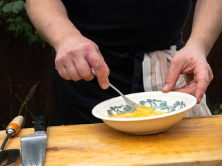 a man in a black apron whips up the yolk of eggs in a plate with a fork.