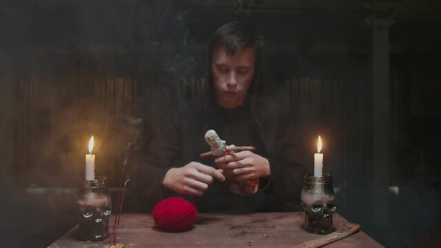 Concentrated mysterious wizard male fortune teller uses voodoo doll and red rope to terrible magic ritual