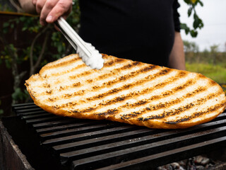 a man turns fried bread on the grill with tongs. picnic making sandwiches in nature.