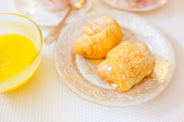 Two crispy croissants on a silver vintage plate and honey in glass on the white sunny table