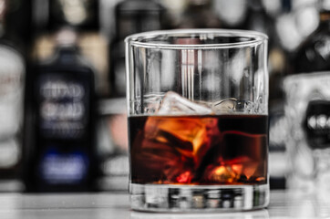 Old fashioned glass with scotch whisky and ice cubes on the bar