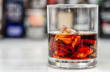 Old fashioned glass with scotch whisky and ice cubes on the bar