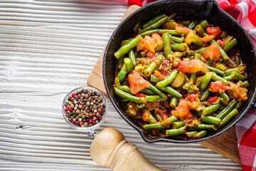 stewed green beans in a cast iron skillet on a white wooden rustic background