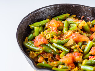 stewed green beans in a cast iron skillet on a white background