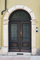 Italian retro wood style front door, the main entrance on the khaki color wall facade. Element of the classic Italian facade and architecture