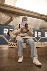 Woman in mask typing a message on her mobile phone while sitting in subway