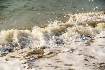 Tides of ocean water or sea water splashing onto the shore of a sandy beach causing white foam and bubbles