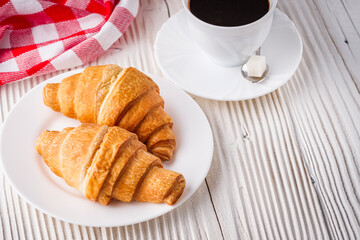 delicious fresh croissant and cup of coffee on a white wooden rustic background