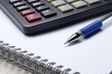 a ballpoint pen and a micro calculator lie on a squared notebook. close-up.