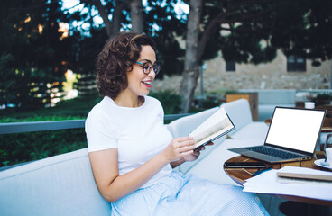 Cheerful woman reading book in outdoor restaurant