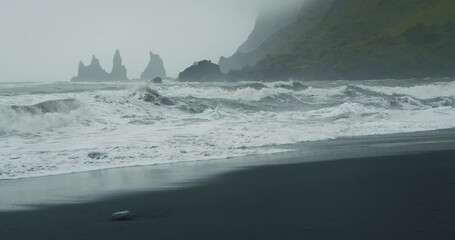 The black sand beach of Reynisfjara with waves hitting the shore on foggy rainy stormy day. Vik, Iceland. - Powered by Adobe