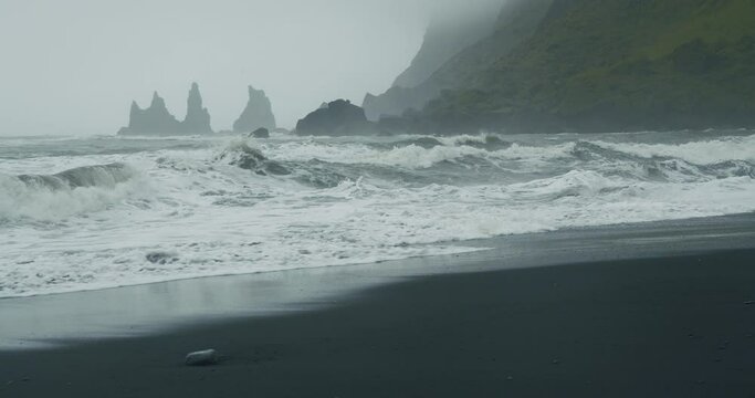 The black sand beach of Reynisfjara with waves hitting the shore on foggy rainy stormy day. Vik, Iceland.
