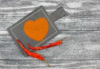 Heart from paprika and two hot chili peppers on the gray background with copy space