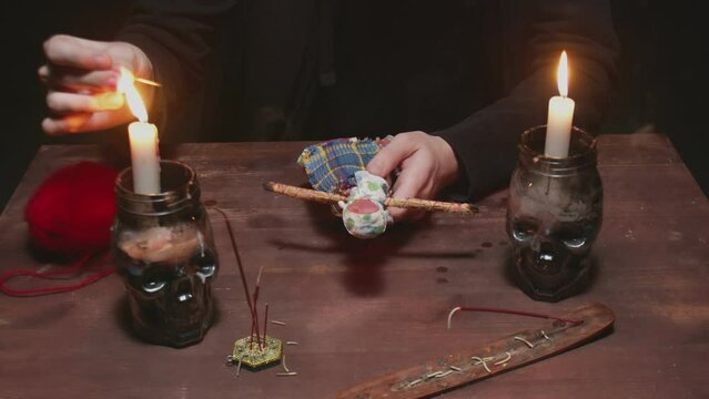 Close up of mysterious wizard male fortune teller sticks a needle into voodoo doll in terrible magic ritual