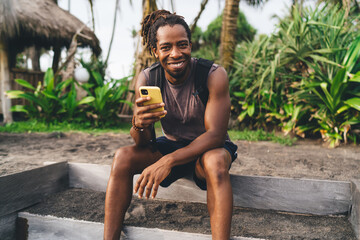 Cheerful black man using smartphone and looking at camera