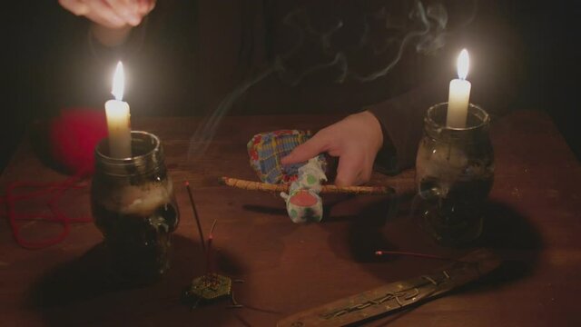 Close up of mysterious wizard male fortune teller sticks a needle into voodoo doll in terrible magic ritual in dark
