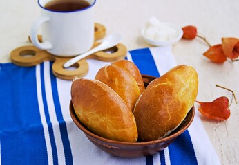 Homemade baked pies from yeast dough with meat in a brown clay bowl on a light concrete background. Russian cuisine.
