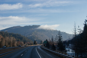 An asphalt road along which cars and trucks go, among the mountains, ahead on the horizon mountains in fog, the sky is covered with clouds. Idaho, USA, 11-23-2019