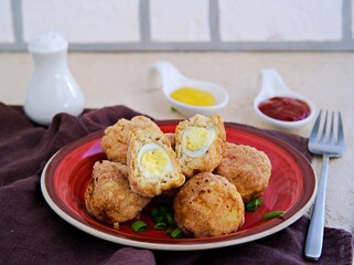 Scottish eggs, boiled quail eggs in minced chicken on a red clay plate on a light concrete background. Can be served as a starter or main course.