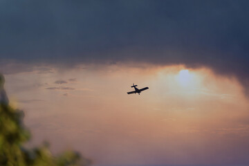 Silhouette of a small plane over a dramatic sky at sunset