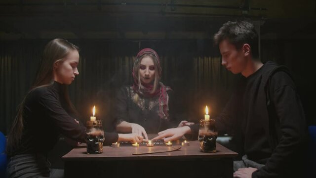Witch female fortune teller tries to speak with ghost. Two women and one man uses Ouija Board Spirit Game
