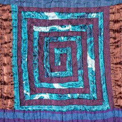 textile background - stitched detail of patchwork fabric with spiral pattern