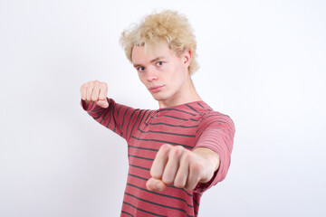 Young handsome Caucasian blond man standing against white background Punching fist to fight, aggressive and angry attack, threat and violence