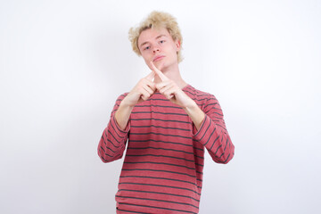 Young handsome Caucasian blond man standing against white background Has rejection angry expression crossing fingers doing negative sign.