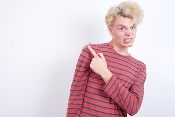 Young handsome Caucasian blond man standing against white background Pointing aside worried and nervous with forefinger, concern and surprise concept.