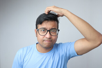 a young indian man in spectacles scratching his head and looking confused and thoughtful