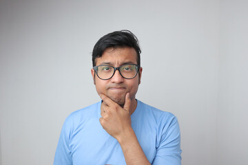 a young indian man in spectacles holding his chin and looking confused and thoughtful