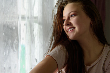Fototapeta premium The girl smiles and looks out the evening window.