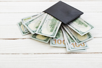 dollars in  black wallet on white wooden background