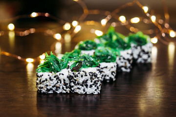 Vegetarian rolls with Chuka seaweed and sesame seeds. On a dark wooden background with lights. Image with selective focus and tinting.