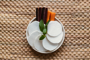 Vegetables on plate with wicker background. Carrots and radishes on a white plate. Healthy...