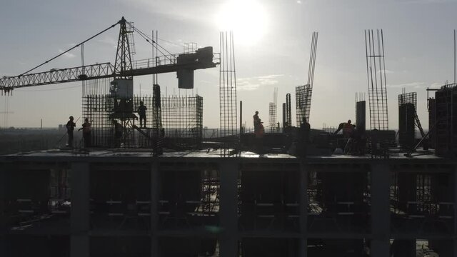 Construction workers (builders) silhouettes are on the rooftop of a residential building under construction (in a course of building). Aerial side view