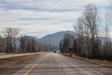 An asphalt road along which cars and trucks go, among the mountains, ahead on the horizon mountains in fog, the sky is covered with clouds. Idaho, USA, 11-23-2019