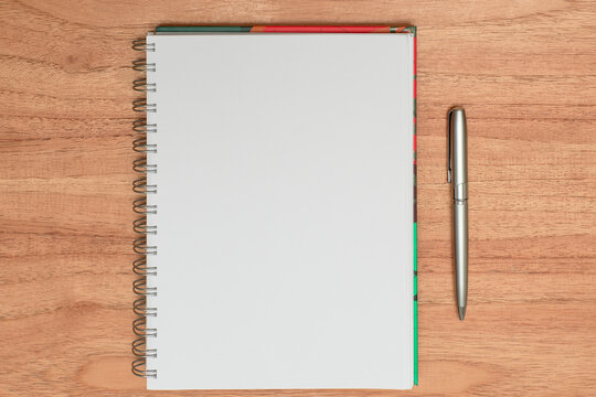 Cuaderno liso blanco con lapicera plateada sobre madera