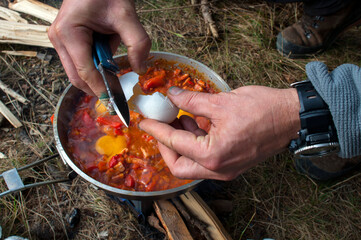 cooking scrambled eggs with vegetables on the fire in the woods