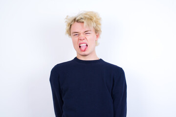 Young handsome Caucasian blond man standing against white background sticking tongue out happy with funny expression. Emotion concept.