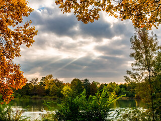 Autumn sketch at lake, sun light breaking through  dark clouds, framing multicolored foliage