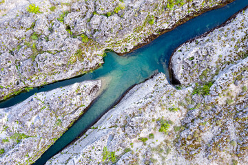 Fork of a narrow mountain river flowing through bare rocky landscape. Stream bed cut deep into...