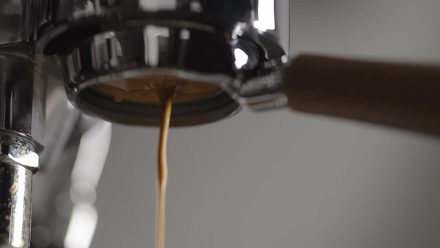 Slow motion low angle spurter shot of espresso extraction from naked portafilter into white cup