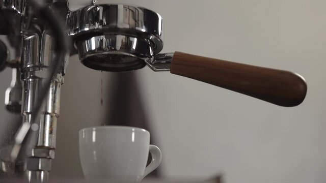 Slow motion low angle shot of espresso extraction from naked portafilter into white cup