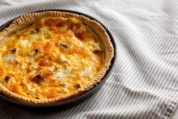 Homemade Bacon Quiche with Eggs and Cheddar Cheese on cloth, low angle view. Copy space.