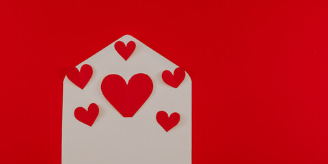 
White envelope and hearts on red.

White envelope and paper hearts on the left on a red background with space for text on the right, top view close-up.