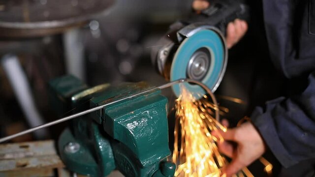 Selective focus of young female blacksmith using hand welding machine to join iron rods in a circular shape with sparks during welding process