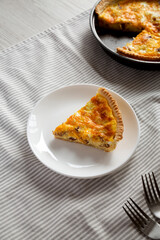 Homemade Bacon Quiche with Eggs and Cheddar Cheese on a white plate, high angle view.