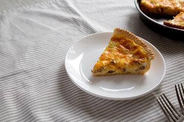 Homemade Bacon Quiche with Eggs and Cheddar Cheese on a white plate, side view. Copy space.