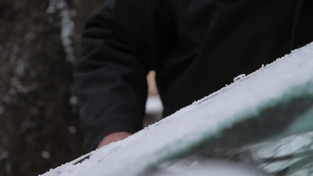 Person hand moves black scraper on car windshield and small ice pieces fall on hood slow motion. Concept weather conditions